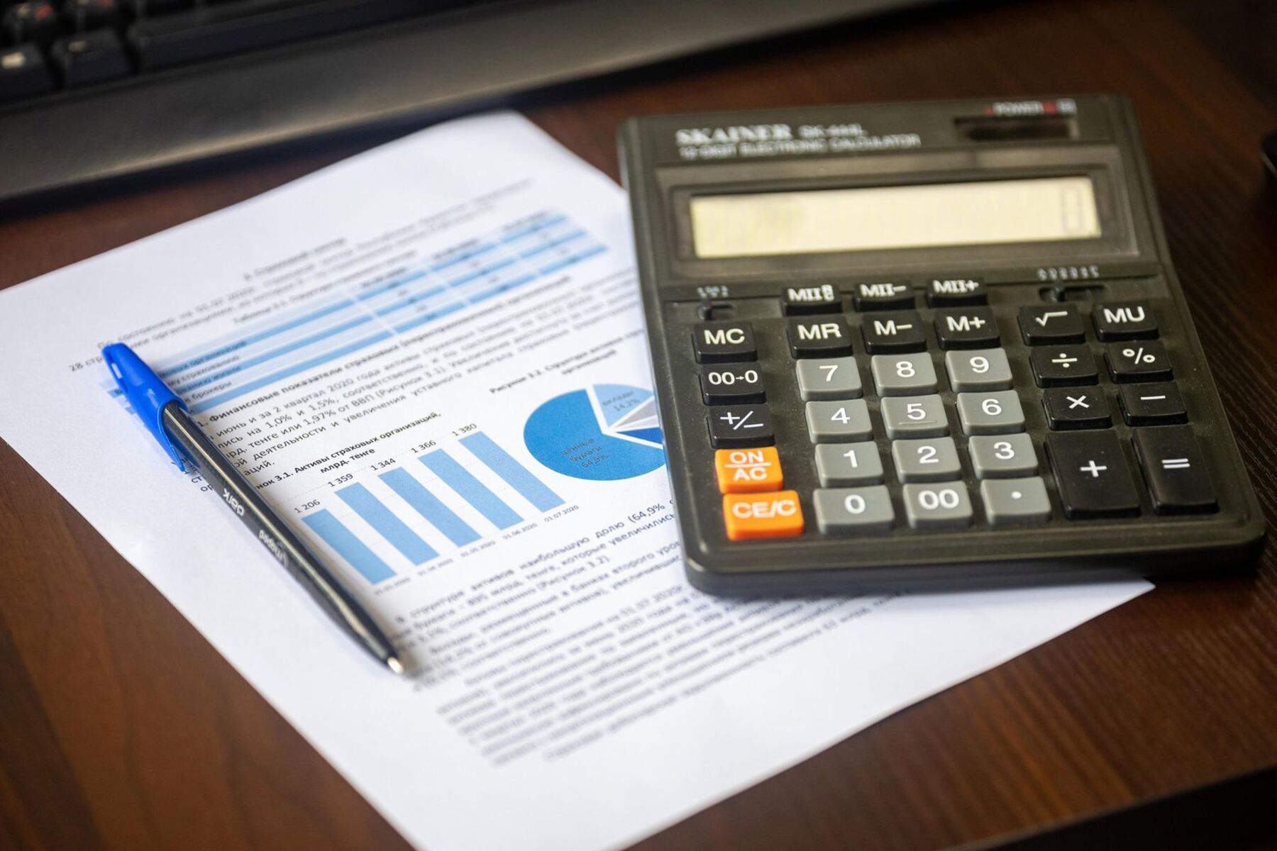 A calculator, pen and printed financial report on a wooden desk